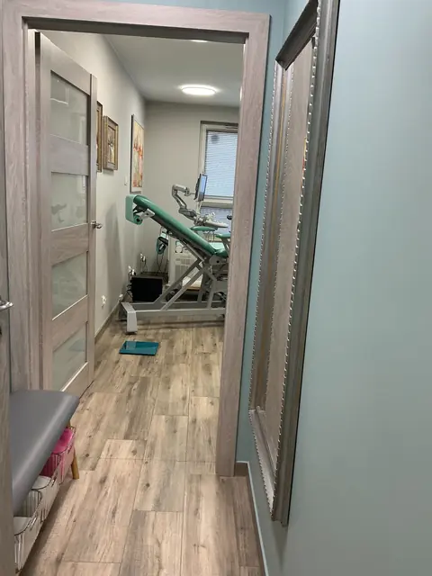 Przejście między pomieszczeniami z widocznym fotelem w gabinecie badań.