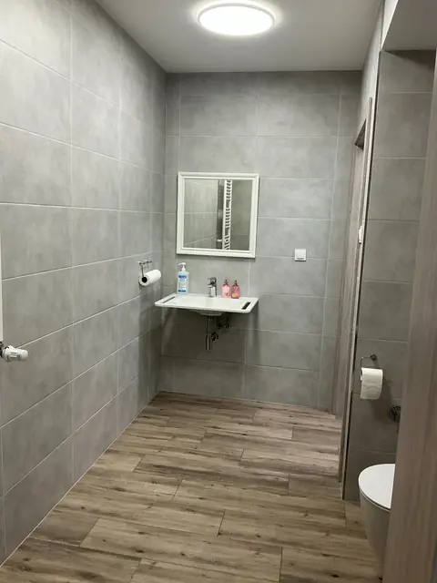Toaleta w gabinecie w Koszalinie z szarymi płytkami, lustrem i umywalką.